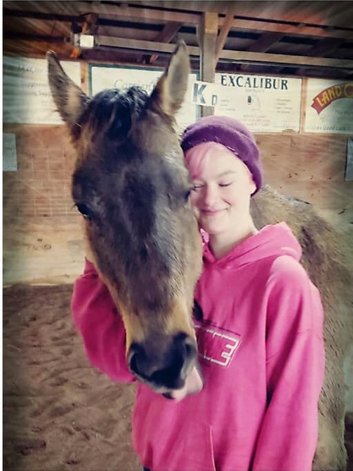 A young woman with her eyes closed, leaning her cheek against a horse’s face